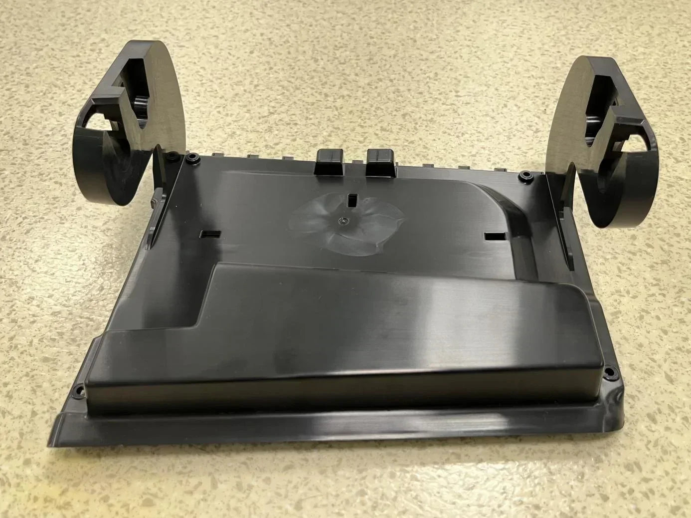 Glossy black injection‑molded plastic industrial spare part on speckled countertop