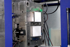 Close-up of a steel two-shot injection mold inside a machine, showing cavities, hoses, sensor blocks, and green status lights above.