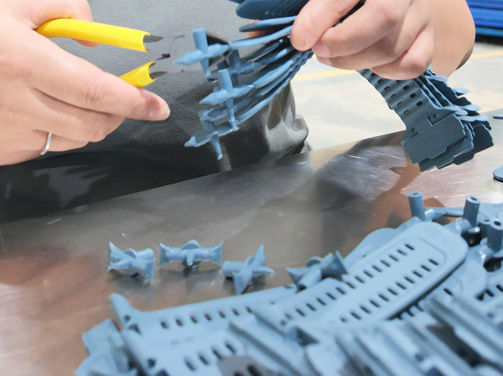 Worker trimming excess material from custom plastic parts during post-processing and quality inspection.