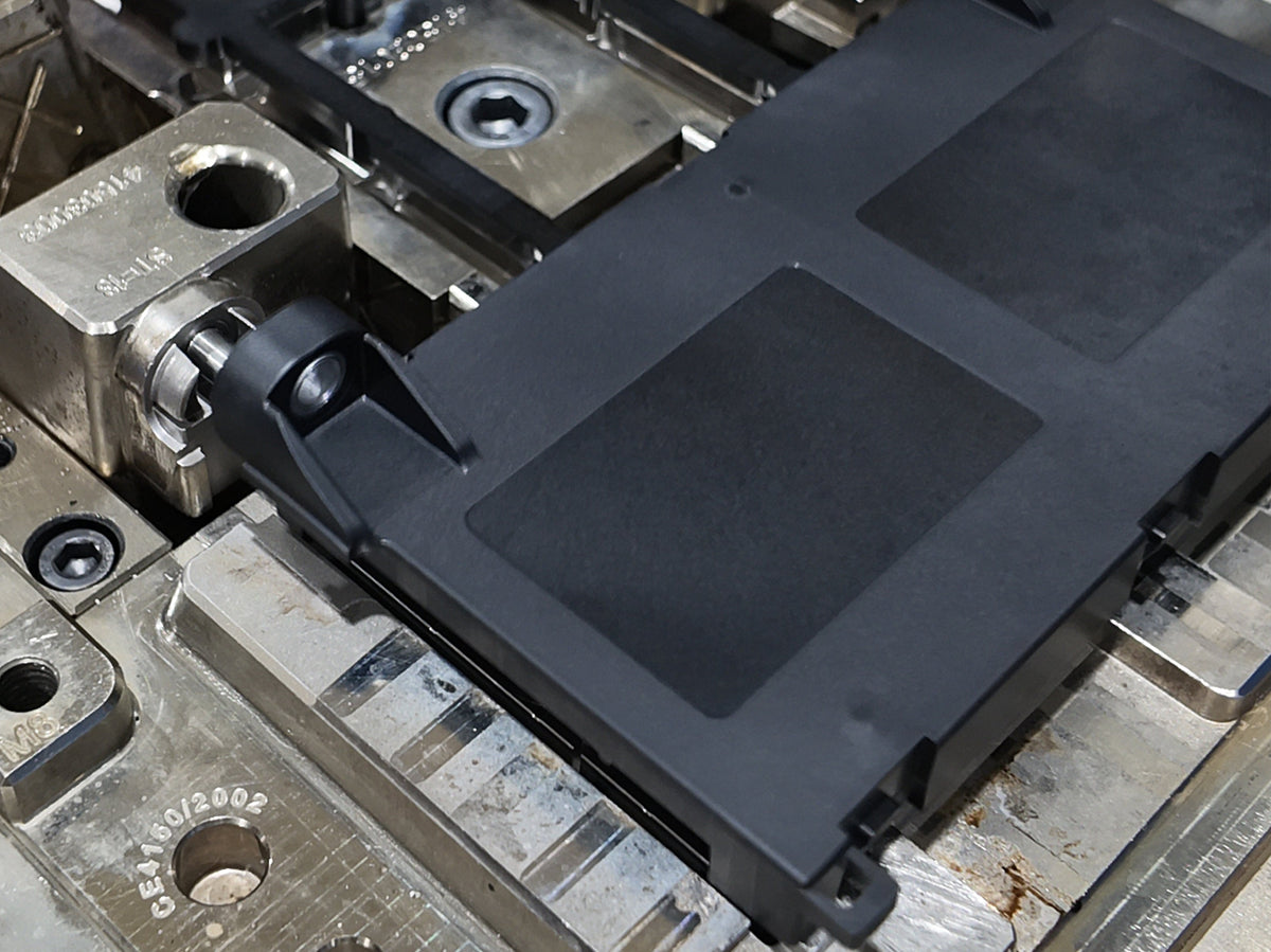 Black custom injection molded plastic component positioned inside a precision manufacturing mold.