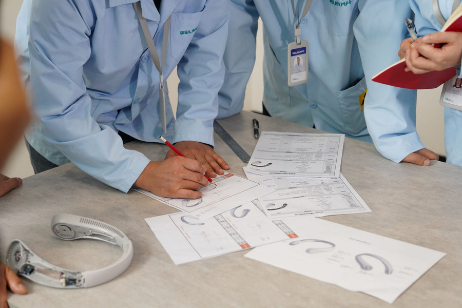 Several Weilan MFG engineers gather to perform early DFM analysis using design drawings and a neck fan prototype.