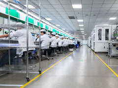 Assembly line workers in white coats seated at a clean manufacturing workstation