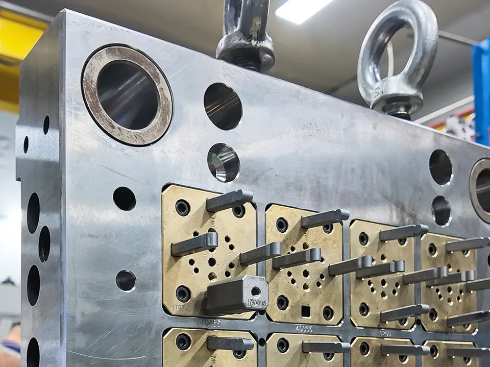 Steel injection mold with brass slide-core inserts, part numbers engraved, and lifting eye bolts.
