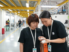 Two female factory workers inspecting finished plastic workpiece inside bright manufacturing workshop
