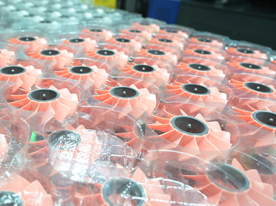 Pink plastic fan parts arranged in clear trays after molding.