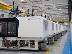 Rows of clean white injection molding machines line a bright factory floor with overhead cranes and organized production equipment nearby.
