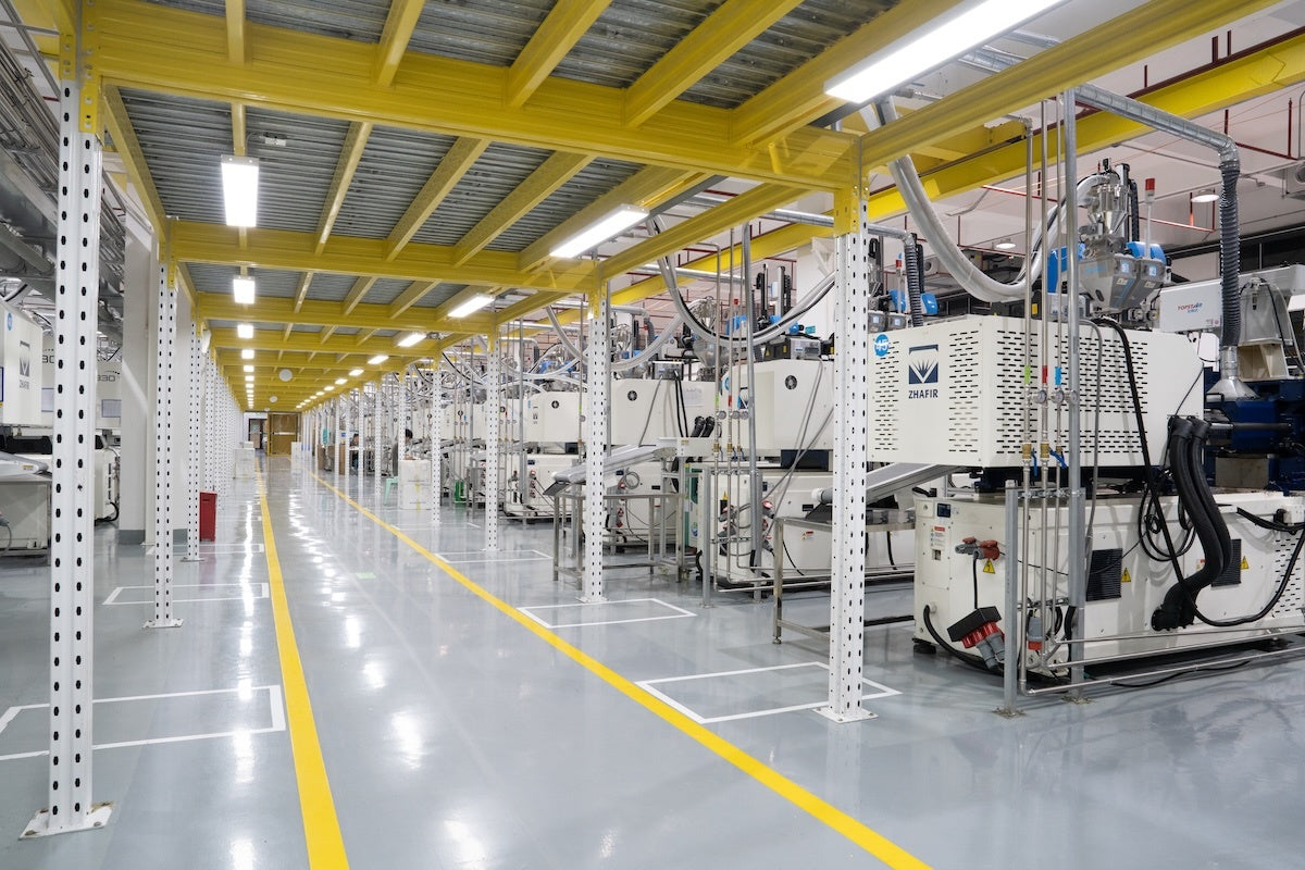 Bright injection molding workshop with long rows of machines, overhead yellow beams, clean floor markings, and organized production lanes for stable manufacturing.