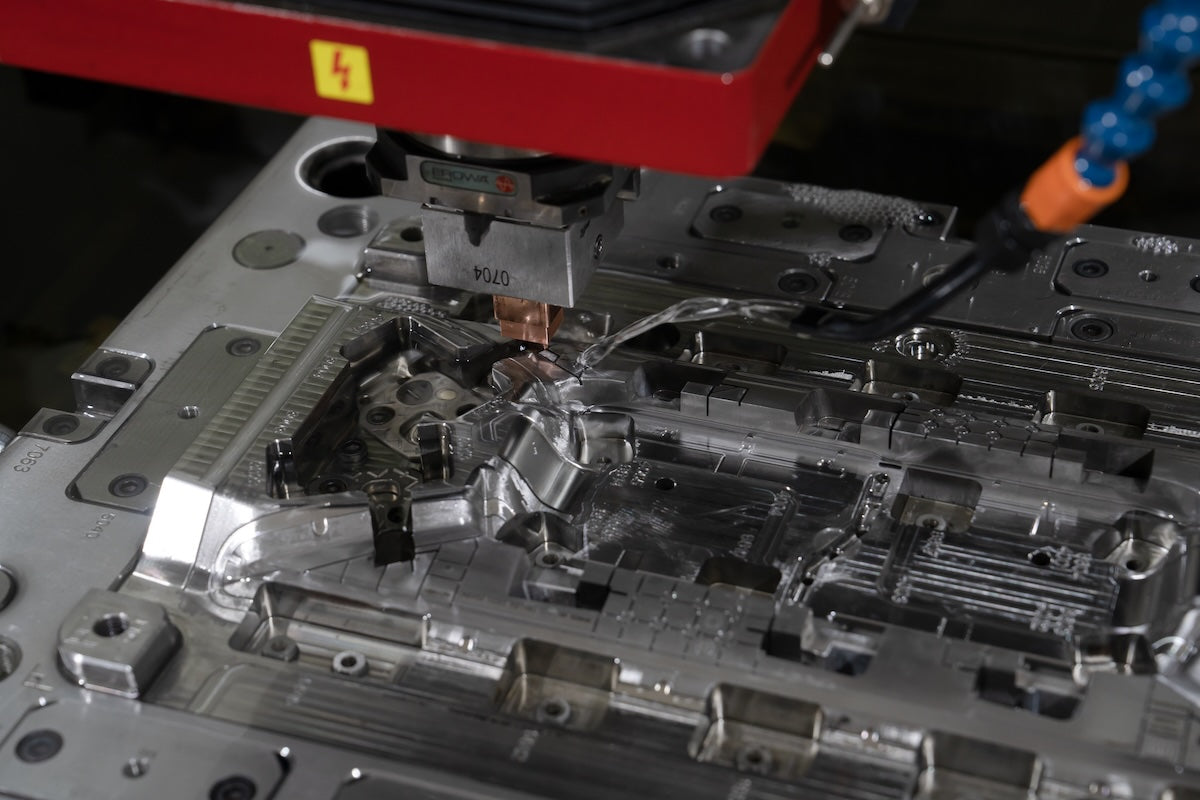 EDM electrode machines a polished complex mold cavity with detailed ribs, slots, and reflective metal surfaces.