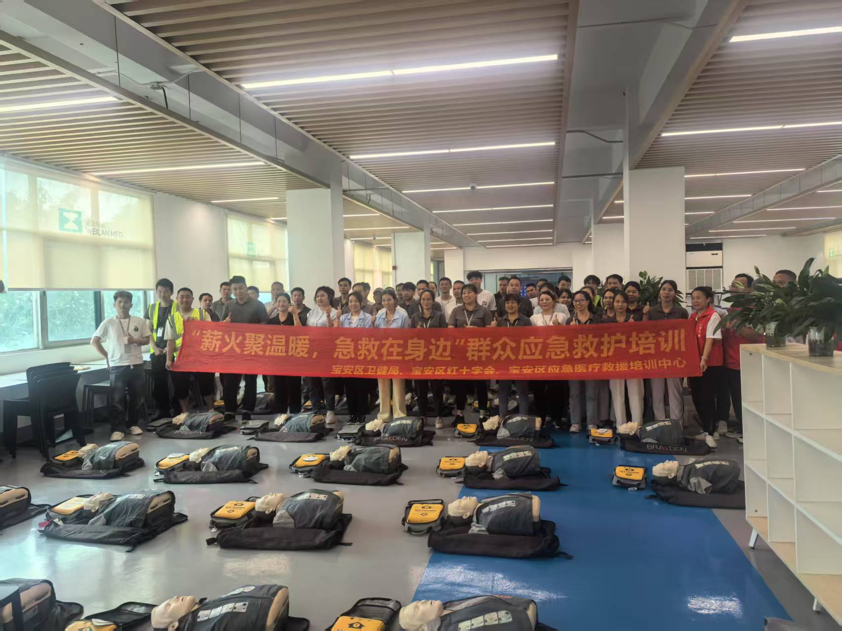 Full group photo of Weilan MFG employees with Red Cross instructors holding a red banner, with CPR manikins and AED units in the foreground